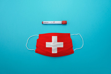 Disposable medical surgical face mask with Switzerland flag superimposed on it with positive COVID-19 test on blue background. Coronavirus (COVID-19) pandemic affects the country. Stay home, stay safe