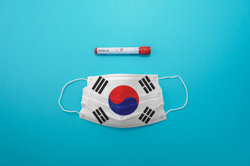 Disposable medical surgical face mask with South Korea flag superimposed on it with positive COVID-19 test on blue background. Coronavirus (COVID-19) pandemic affects the country. Stay home, stay safe
