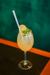 Cold summer alcohol cocktail with ice and orange in a tall glass on wooden table on blurred restaurant background.