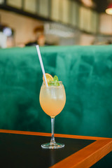 Cold summer alcohol cocktail with ice and orange in a tall glass on wooden table on blurred restaurant background.