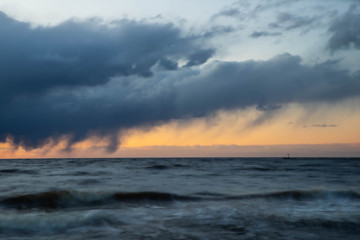 Fototapeta na wymiar Sea waves of Baltic sea at long exposure. Scenic sunset over the water. Lightouse.