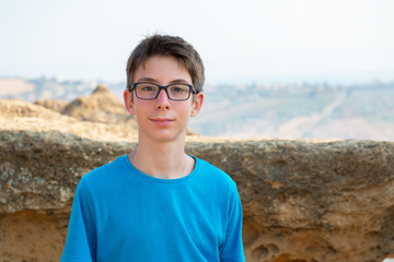 Handsome cheerful teen boy with glasses against landscape of Sicily. Travel destination. Tourism