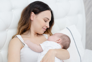 Obraz na płótnie Canvas Closeup portrait of cheerful young mother with adorable newborn baby having fun at home, child care, happy parenthood, love concept