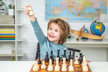 Thinking child. Kid Playing Chess. Cheerful smiling little boy sitting at the table and evincing gladness while playing chess.
