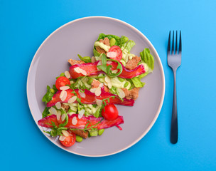 Fresh salad with smoked salted salmon, tomatoes and pumpkin seeds. Served on a gray plate over gray texture background.