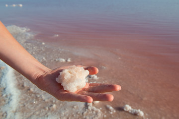 Fototapeta na wymiar Boy's hand full of salt against of salty pink lake. Salt mining. Extremely salty pink lake, colored by microalgae with crystalline salt depositions in Torrevieja, Spain