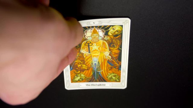 A hand lays out a tarot card, Thoth Tarot, "The Hierophant" on black tablecloth. Tokyo, Japan. March, 2020. Camera fixed, close-up, high angle view.