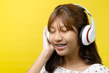 Happy Asian teenager girl wearing headphone on yellow background.