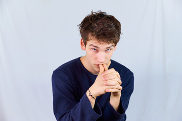 Tense, desperate young man crouched with hunched shoulders, biting the thumbnails of his folded...
