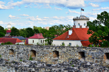 Cesis, Latvia - The stone wall of the old castle beyond which is visible the Cessian new castle, a historical and art museum, a building with a neo-Gothic tower, a blue sky with clouds.