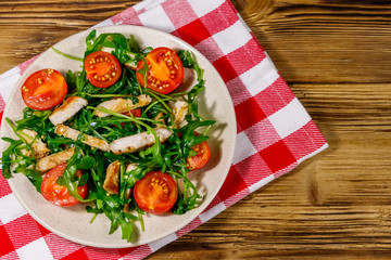 Tasty salad of fried chicken breast, fresh arugula and cherry tomatoes on wooden table. Top view