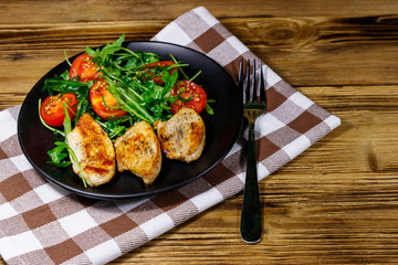 Fried chicken breast with salad of fresh arugula and cherry tomatoes on wooden table