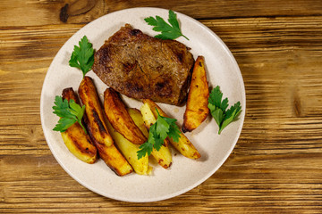 Fried beef steak with potato wedges on wooden table. Top view