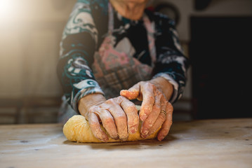 Close up old woman hands kneading dough to prepare fresh Italian pasta homemade on a wooden cutting...
