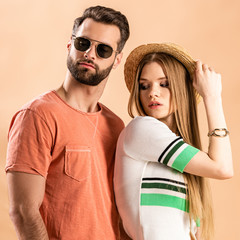 beautiful fashionable couple posing in summer clothes, straw hat and sunglasses on beige