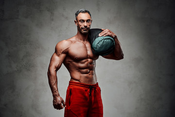 Buffed sportsman posing in a dark studio with a weight bag looking strong