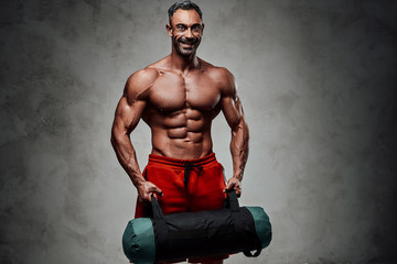 Close-up photo of a sportsman, flexing with a sand bag in a dark studio