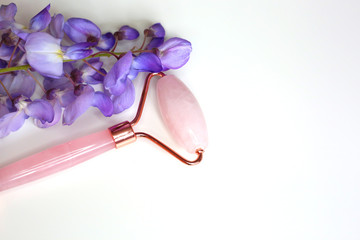 Pink quartz face roller massager for skin treatment on whit background. Jade roller. Home spa settings. 