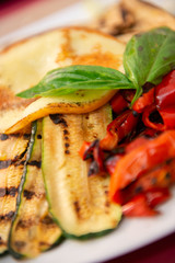 Delicious tasty traditional italian grilled vegetables cooked in restaurant, detail, soft focus. Bell pepper, basil; Mozzarella cheese and squash on plates