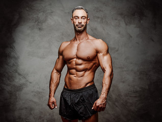 Shirtless adult male bodybuilder posing for a photoshoot shirtless in a dark studio