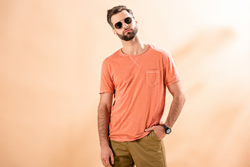 fashionable young man posing in shorts, summer t-shirt and sunglasses on beige