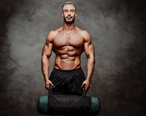Fototapeta na wymiar Handsome adult sportsman wearing sportswear posing for a camera while holding a weight bag