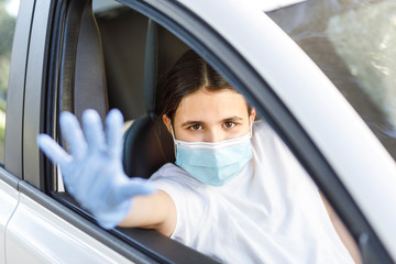 bambina con i capelli neri indossa una mascherina facciale e guanti in lattice per proteggersi fa stop con la mano dall'abitacolo di un automobile