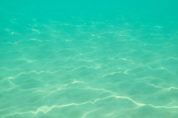 Fototapeta na wymiar Underwater. Sun glare at the bottom of the sea. Waves underwater and rays of sunlight shining through. Deep turquoise blue sea. Ocean. Transparent water and light at sand.