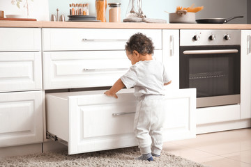 Little African-American baby playing in kitchen. Child in danger