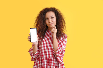 Thoughtful young African-American woman with mobile phone on color background