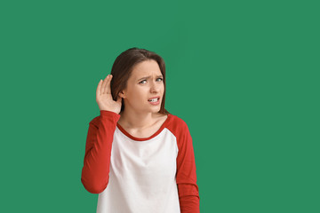 Young woman trying to hear something on color background