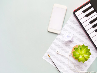 Top view of piano keyboard with sell phone, headphones, note paper and plant on grey background....