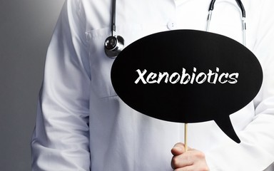 Xenobiotics. Doctor in smock holds up speech bubble. The term Xenobiotics is in the sign. Symbol of illness, health, medicine