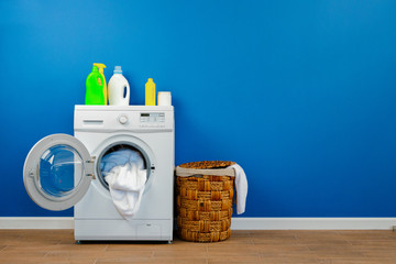 Washing machine with laundry on blue wall background, close up.