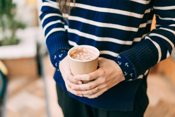 Closeup girl holding a mug with cocoa and marshmallows. A delicious drink in a disposable cup that...