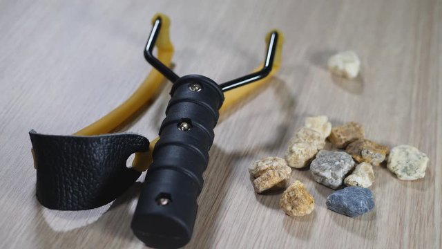 Stone and rock with slingshot small hand-powered projectile weapon. Classic form Y-shaped frame held in off hand with two rubber strips attached to uprights. Pocket that holds projectile
