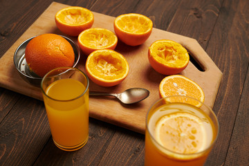 Fresh orange fruits whole and squeezed on a wooden table, cutting board - natural and healthy food. Glass of fruit cocktail.