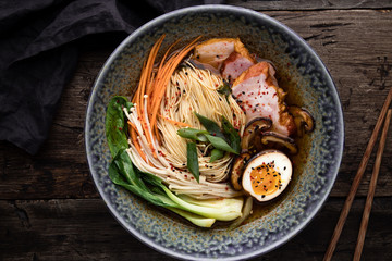 Bowl of ramen soup with pork, shiitake and enoki mushrooms, marinated egg and vegetables.
