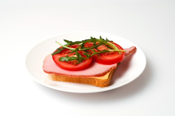 Sandwich of balyk, cheese, bread, tomatoes and arugula on a white plate on a plate