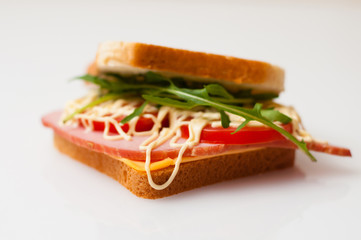 Sandwich made of bread for toast, balyk, tomatoes, arugula, cheese and mayonnaise on white plate side view