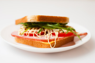 Tasty sandwich with ham or balyk, tomato, arugula, cheese, mayonnaise and white bread for toast on a plate on a white background