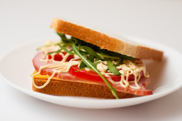 Tasty sandwich with ham or balyk, tomato, arugula, cheese, mayonnaise and white bread for toast on a plate on a white background