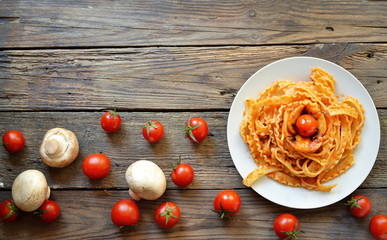 Pasta in a white plate. Pasta with tomato sauce, mushrooms with cherry tomatoes. Wooden background. Free space for text.