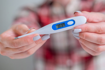 Woman hands showing white digital medical thermometer with high temperature - close up, selective focus, front view. Healthcare, measurement, disease, covid 19, infection, coronavirus concept