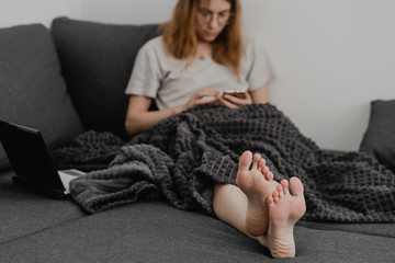 Fototapeta premium Attractive Young Woman Working from Home - Female Entrepreneur Sitting on sofa with Laptop Computer and Checking Cell Phone from Comfort of Home