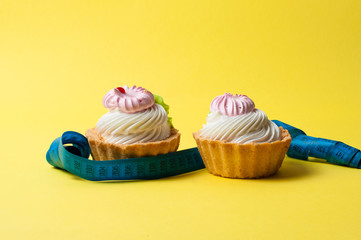 Two cakes and a centimeter on yellow background. Concept of weight control and healthy eating.