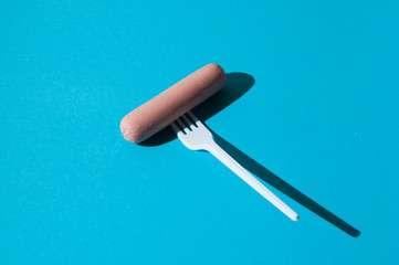 Raw sausage on a blue background with a plastic fork