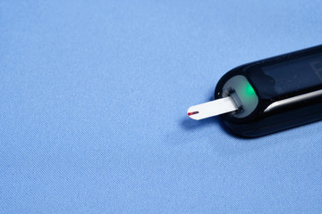The glucometer with the test strip on a blue background. space for text