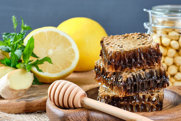honey in honeycombs on a wooden plate and honey with nuts with lemon and ginger in rustic style on...