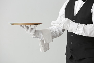 Male waiter with empty tray on grey background